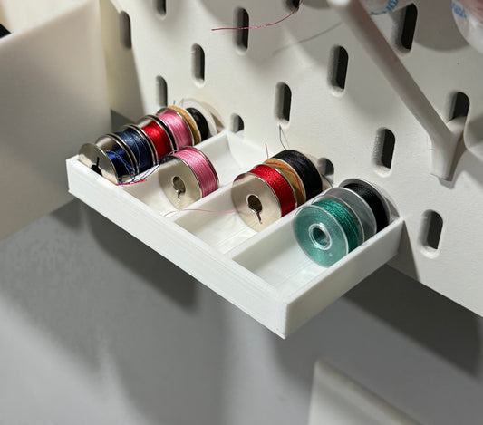 Skadis Bobbin holder in white attached to a pegboard.